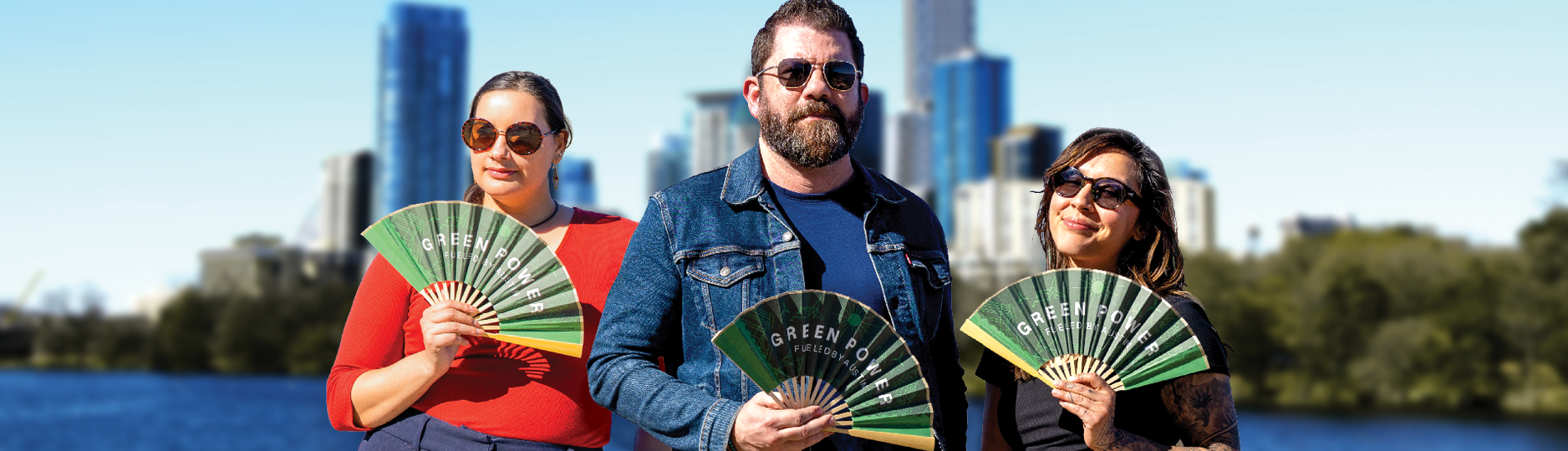 Three people holding Green Power fans with downtown skyline behind
